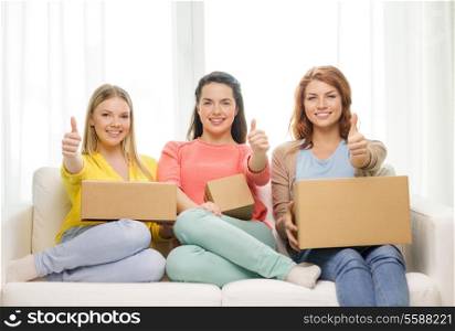 transportation, post and friendship concept - three smiling teenage girls with cardboard boxes at home showing thumbs up