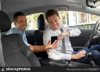 transportation, taxi and technology concept - middle aged male passenger on back seat showing his smartphone to car driver. male passenger showing smartphone to car driver