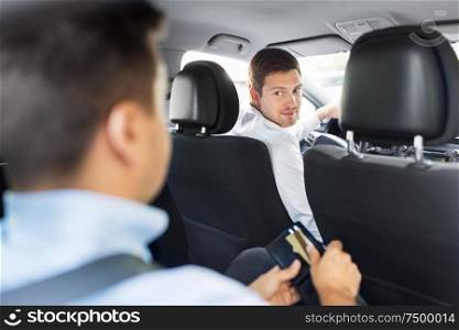 transportation, vehicle and payment concept - male car driver looking at passenger with credit card in wallet. male car driver looking at passenger with wallet