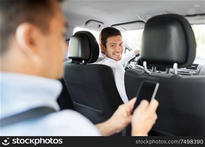 transportation, vehicle and people concept - male car driver looking at passenger with smartphone sitting on back seat. male car driver and passenger with smartphone