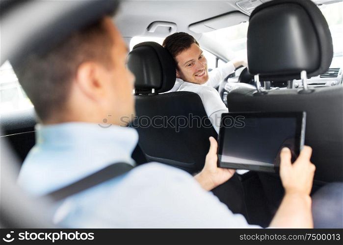 transportation, vehicle and people concept - male car driver looking at passenger with tablet pc computer sitting on back seat. male car driver and passenger with tablet pc