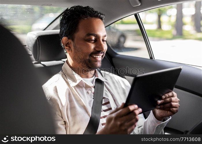transportation, vehicle and people concept - smiling indian male passenger with tablet pc computer in taxi car. indian male passenger with tablet pc in taxi car