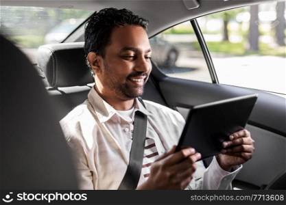 transportation, vehicle and people concept - smiling indian male passenger with tablet pc computer in taxi car. indian male passenger with tablet pc in taxi car