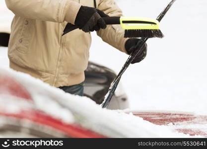 transportation, winter and vehicle concept - closeup of man cleaning snow from car windshield with brush