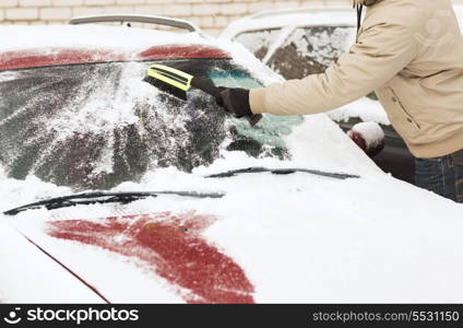 transportation, winter and vehicle concept - closeup of man cleaning snow from car windshield with brush