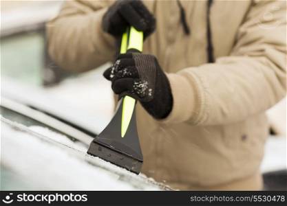 transportation, winter and vehicle concept - closeup of man scraping ice from car windshield with brush