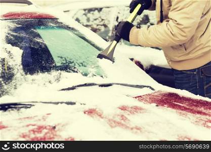 transportation, winter and vehicle concept - closeup of man scraping ice from car windshield with brush