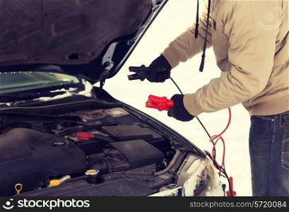 transportation, winter and vehicle concept - closeup of man under bonnet with starter cables