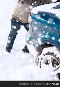 transportation, winter, people and vehicle concept - closeup of man pushing car stuck in snow