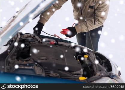 transportation, winter, people and vehicle concept - closeup of man under bonnet with starter cables