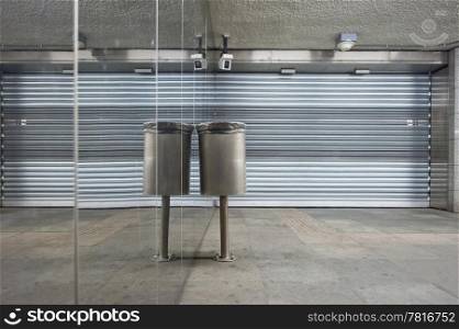 Trash can and closed store front shutters along a mirror wall in a deserted subway station