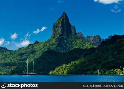 Travel and Stock Photography. View from the water of the tropical bay on Moorea with a sailboat anchored. Moorea Island Roto Nui Volcanic Mountain pushes towards the sky.