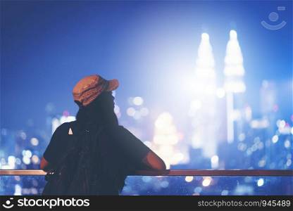 Travel and technology. Young woman taking photo with her smartphone of Petronas Twins Towers in Kuala-Lumpur at evening