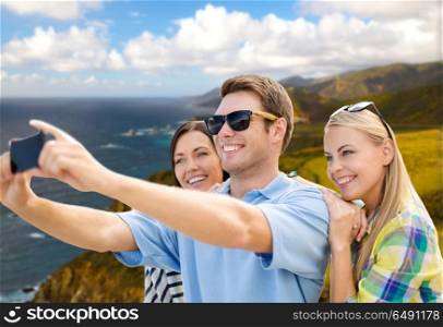 travel and tourism concept - group of happy friends taking selfie by cell phone over big sur coast of california background. group of happy friends taking selfie by cell phone. group of happy friends taking selfie by cell phone