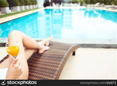 travel and vacation concept - close up of young woman relaxing at a pool in summer with orange juice, selective focus