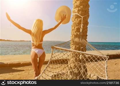 Travel and vacation concept - Woman standing with arms raised up near hammock on the beach.. Travel and vacation concept - Woman standing with arms raised up near hammock on the beach
