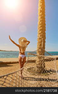 Travel and vacation concept - Woman standing with arms raised up near hammock on the beach.. Travel and vacation concept - Woman standing with arms raised up near hammock on the beach