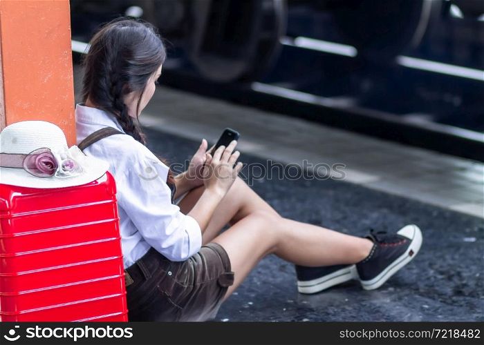 Travel asian woman pregnant look at the Smartphone with a red suitcase at railway station,traveler with backpack in summer Holiday concept Thailand