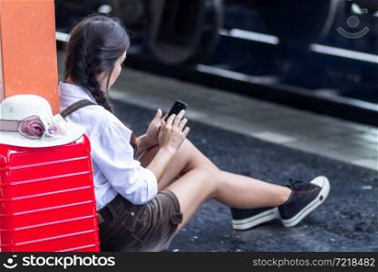 Travel asian woman pregnant look at the Smartphone with a red suitcase at railway station,traveler with backpack in summer Holiday concept Thailand