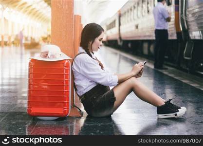 Travel asian woman pregnant look at the Smartphone with a red suitcase at railway station.