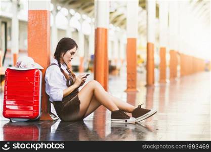 Travel asian woman pregnant look at the Smartphone with a red suitcase at railway station.