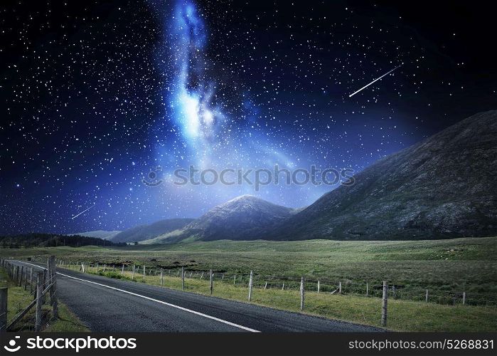 travel, astronomy and landscape concept - landscape with asphalt road and mountains over night sky or space with shooting stars background. night landscape of road and mountains over space