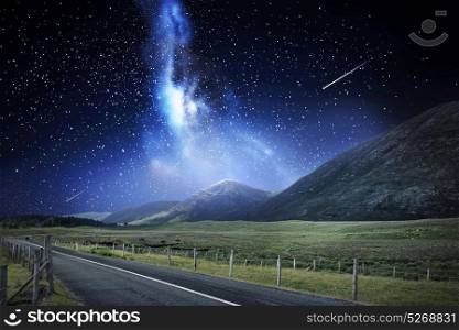 travel, astronomy and landscape concept - landscape with asphalt road and mountains over night sky or space with shooting stars background. night landscape of road and mountains over space