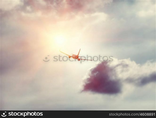 Travel background, silhouette of an airplane in the sky flies towards sun light, modern fast aircraft over cloudy and sunny skies, luxury airlines, transportation and airlift industry