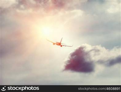 Travel background, silhouette of an airplane in the sky flies towards sun light, modern fast aircraft over cloudy and sunny skies, luxury airlines, transportation and airlift industry
