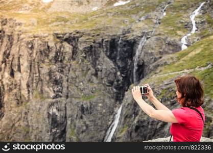 Travel, beauty in nature. Tourist woman looking at mountains, taking picture with camera from Trollstigen viewing point, Norway. Tourist woman on Trollstigen viewpoint in Norway