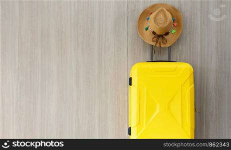Travel bright yellow wheeled luggate and brown straw cowgirl hat with colorful tassel on brown wooden wall background with copy space. Travel and summer holiday concept
