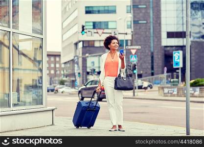 travel, business trip, people and technology concept - happy young african american woman with travel bag and smartphone on city street