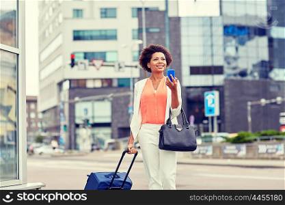 travel, business trip, people and technology concept - happy young african american woman with travel bag and smartphone on city street