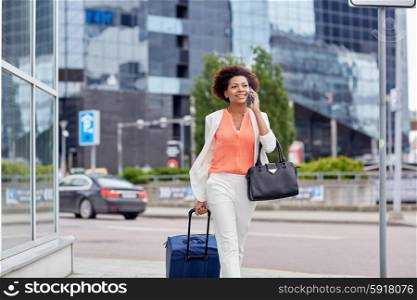 travel, business trip, people and technology concept - happy young african american woman with travel bag walking down city street and calling on smartphone