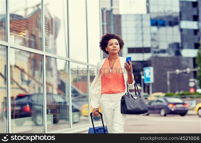 travel, business trip, people and technology concept - young african american woman with travel bag and smartphone on city street
