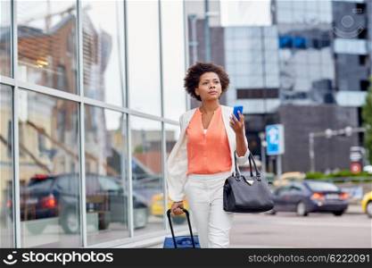 travel, business trip, people and technology concept - young african american woman with travel bag and smartphone on city street