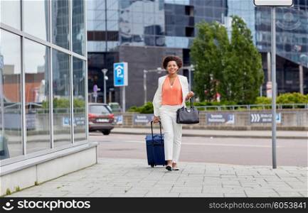travel, business trip, people and tourism concept - happy young african american woman with travel bag walking down city street
