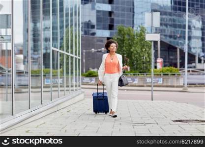 travel, business trip, people and tourism concept - happy young african american woman with travel bag walking down city street