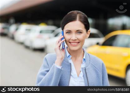 travel, business trip, people and tourism concept - smiling young woman calling and talking on smartphone over taxi station or city street