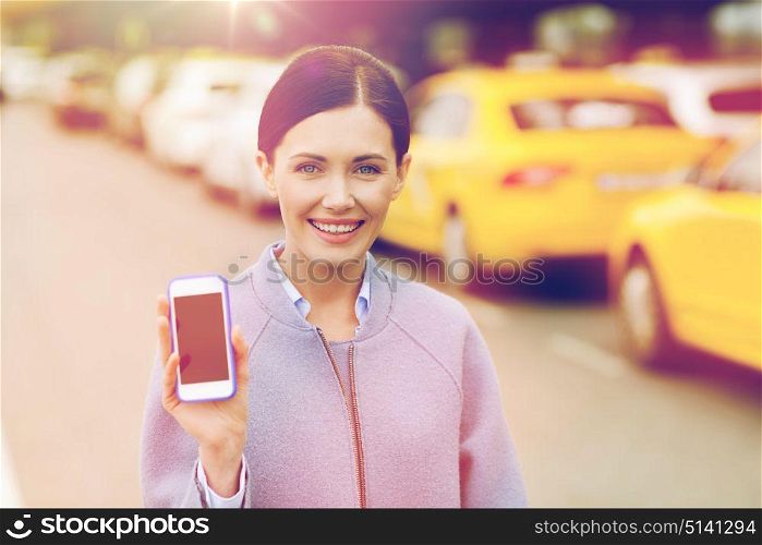 travel, business trip, people and tourism concept - smiling young woman showing smartphone blank screen over taxi station or city street. smiling woman showing smartphone over taxi in city
