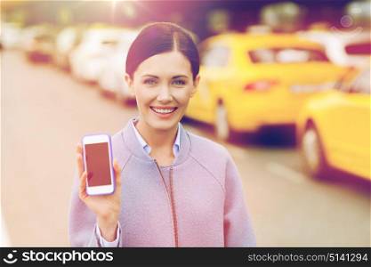 travel, business trip, people and tourism concept - smiling young woman showing smartphone blank screen over taxi station or city street. smiling woman showing smartphone over taxi in city