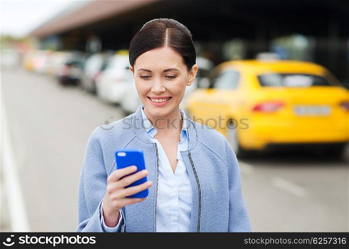 travel, business trip, people and tourism concept - smiling young woman with smartphone over taxi station or city street