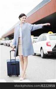 travel, business trip, people, gesture and tourism concept - smiling young woman with travel bag catching taxi at airport terminal or railway station
