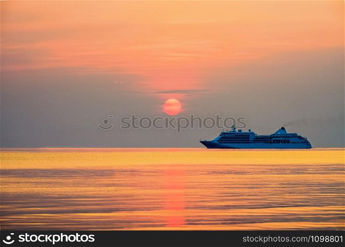 Travel by Cruise ship in the ocean, large luxury passenger boat is sailing on the bright sea, red sun in the colorful sky is yellow, orange, beautiful nature landscape at sunset or sunrise background. Travel by Cruises ship in the ocean at sunset