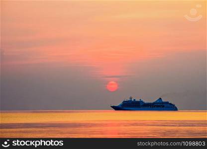 Travel by Cruise ship in the ocean, large luxury passenger boat is sailing on the bright sea, red sun in the colorful sky is yellow, orange, beautiful nature landscape at sunset or sunrise background. Travel by Cruises ship in the ocean at sunset