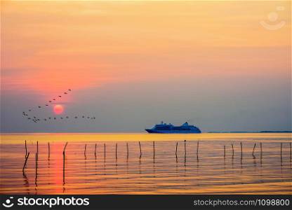 Travel by Cruises ship in the ocean large luxury passenger boat is sailing on the sea, flock birds flying in a line at colorful sky, beautiful nature landscape, red sun at sunset or sunrise background. Travel by Cruises ship in the ocean at sunset