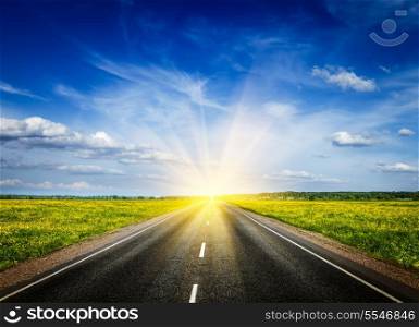 Travel concept background - road in blooming spring meadow on sunset