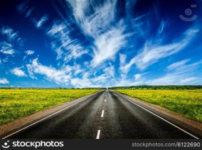 Travel concept background - road in blooming spring meadow. Road in blooming spring meadow