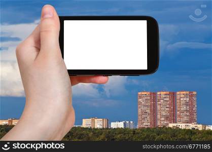 travel concept - hand holds smartphone with cut out screen and dark blue sky over urban houses on background