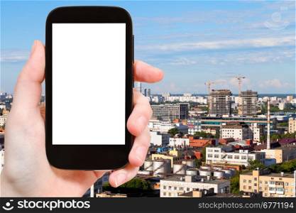 travel concept - hand holds smartphone with cut out screen and urban development on background